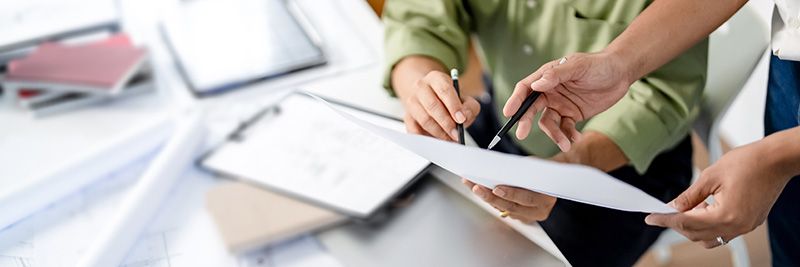 @ business people pointing their pens at a paper discussing the contents